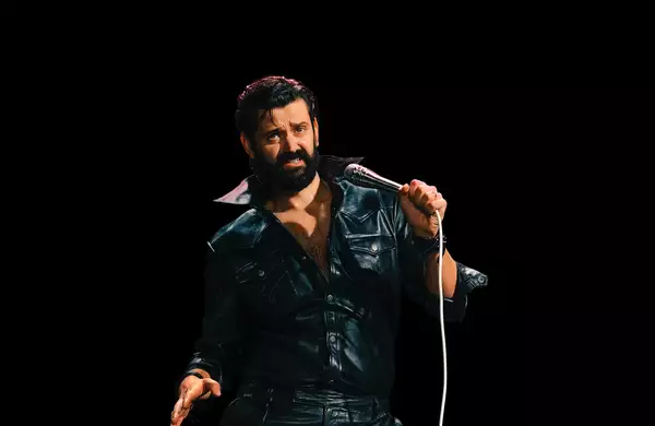 Fin Taylor wearing a black leather outfit and holding a microphone on a black background