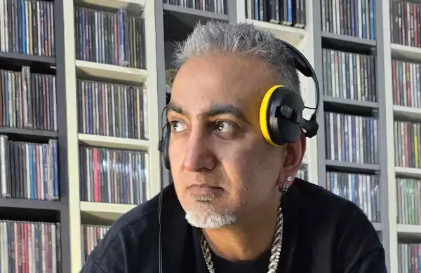 Desi Fusion DJ wearing headphones and stood in front of shelves of records