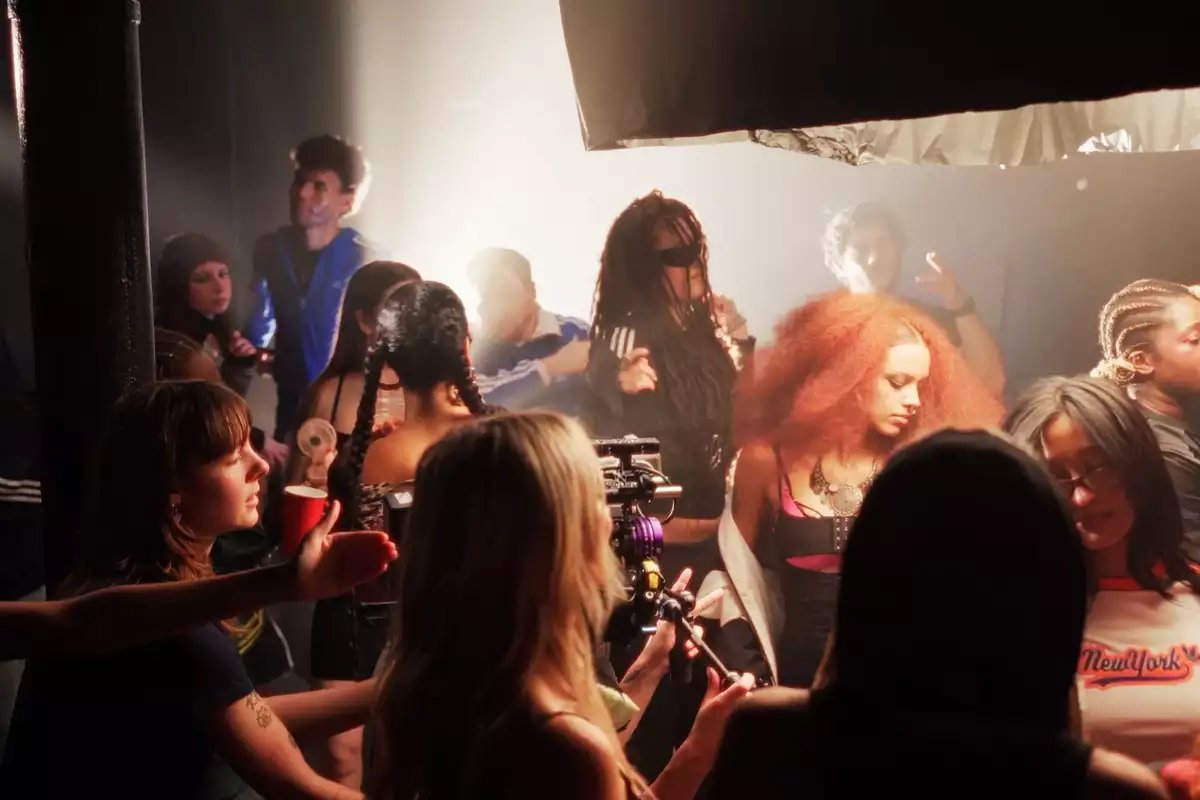 A still from the 'Meet the cohort' video showing a crowded room of people chatting with cameras
