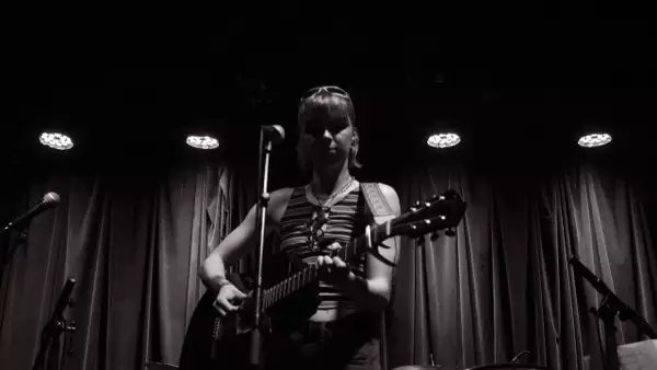 Black and white photograph of Rebecca Spooner on stage playing guitar and singing