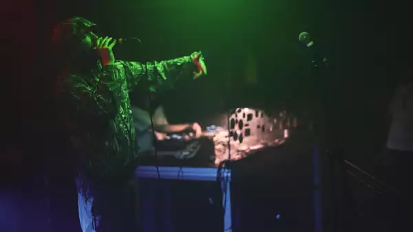 Charlie Boy Manson performing into a microphone on stage in a dimly lit room