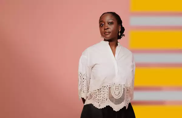 Composer Cassie Kinoshi stands in front of a pink and yellow background