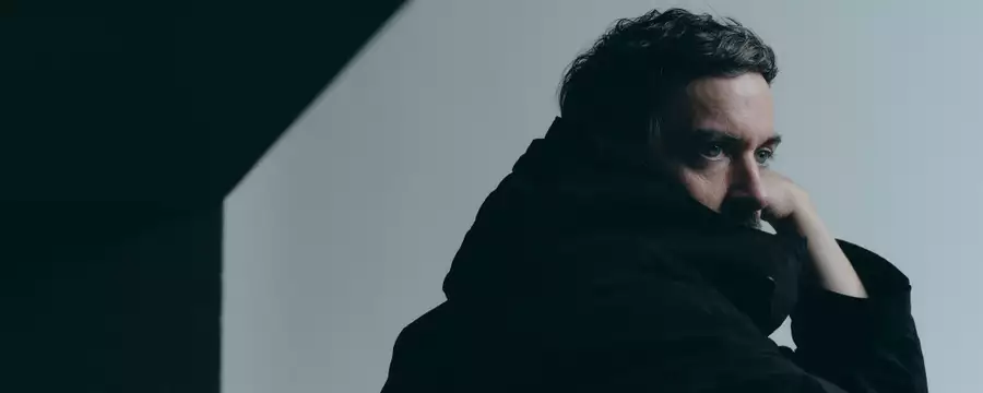 Bonobo wearing a black jacket looking to the side, with a shadow on the wall behind him
