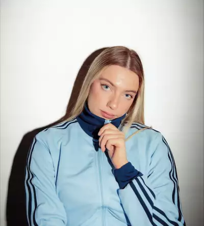 Photo of Amy Parton on a white background wearing a zipped up light blue Adidas tracksuit top