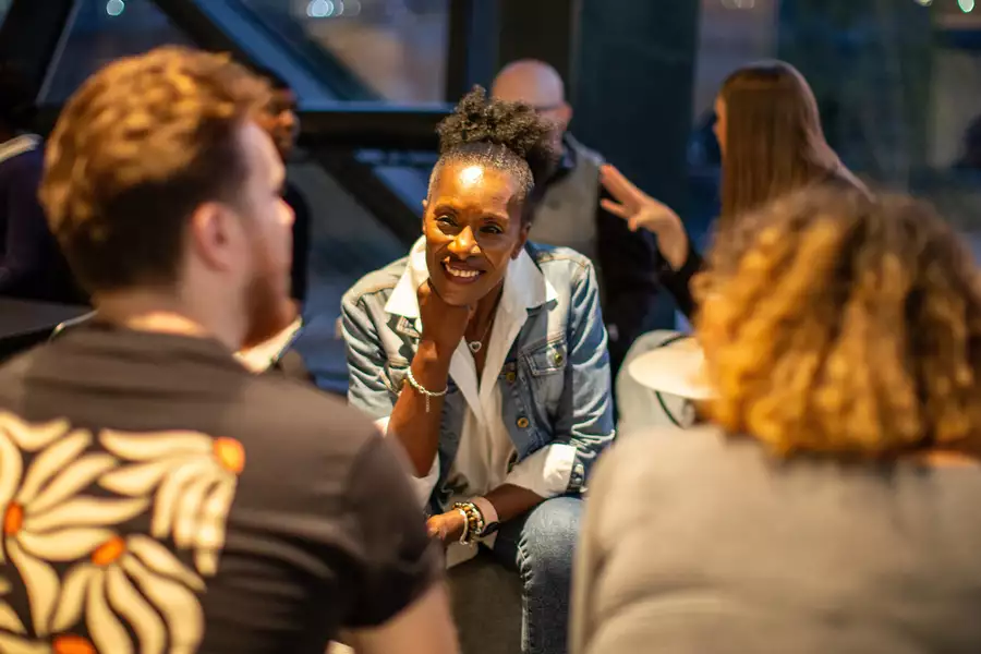 A person smiling in conversation with two other people, who have their backs turned to the camera