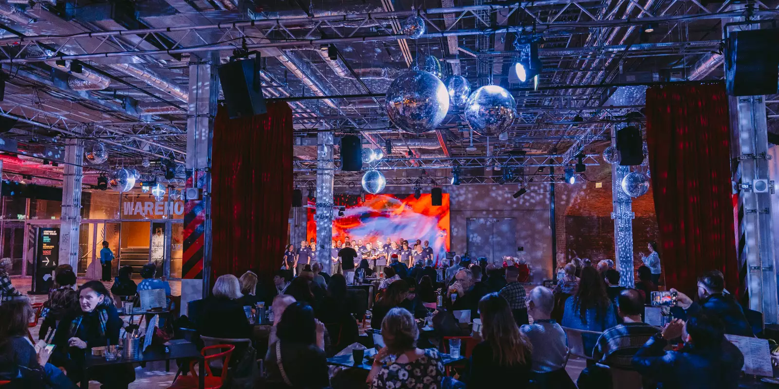 A crowd of people in the Social watching a performance on stage, with festive decorations around them