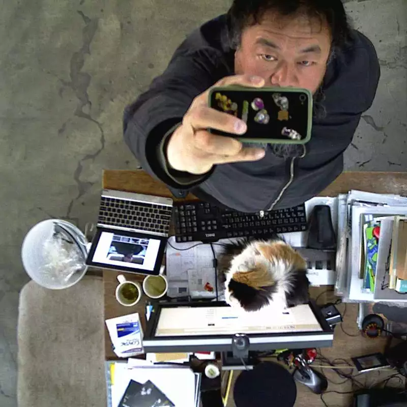 Ai Weiwei filming himself on a phone camera from above, next to a desk