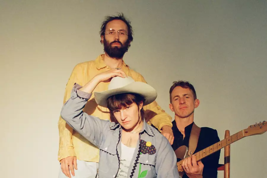 Three members of Big Thief on a white background. Adrianne Lenker is wearing a white cowboy hat.