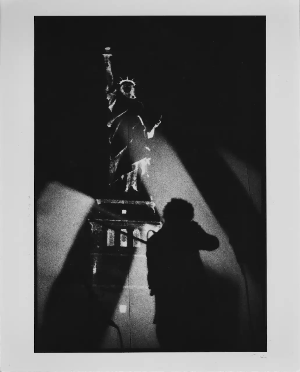 Black and white still from Laurie Anderson's United States Parts 1–4, showing Laurie stood on stage in front of the Statue of Liberty