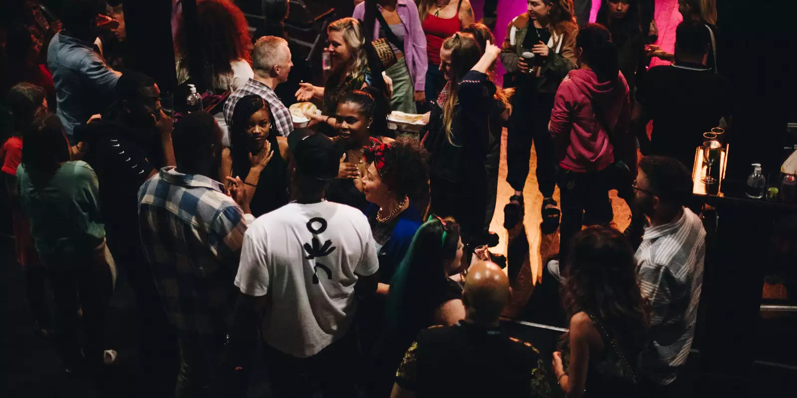 Groups of people talk and mingle in a relaxed atmosphere at an indoor venue with soft lighting.