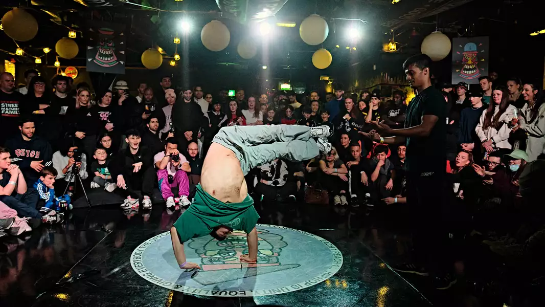 Breakdancer performing a handstand move in a crowded battle setting.
