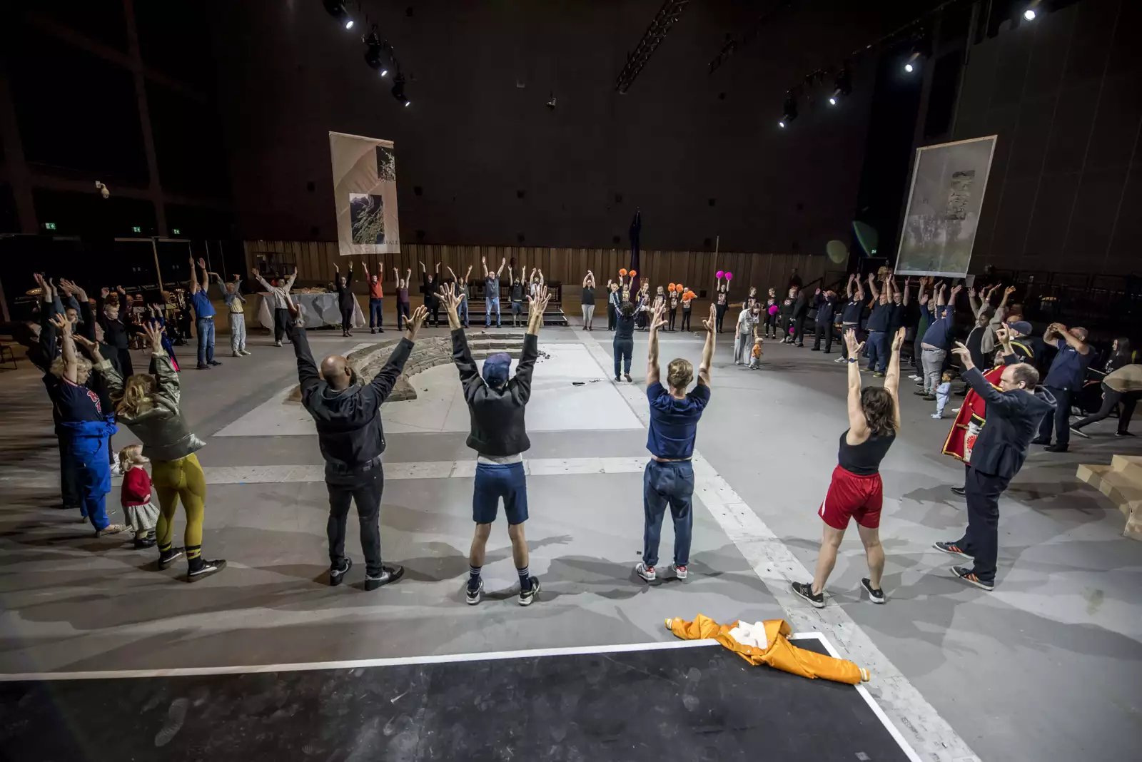 A large group of people with their hands in the air stood in a circle around a clay installation – for the June 2024 Artist Takeover