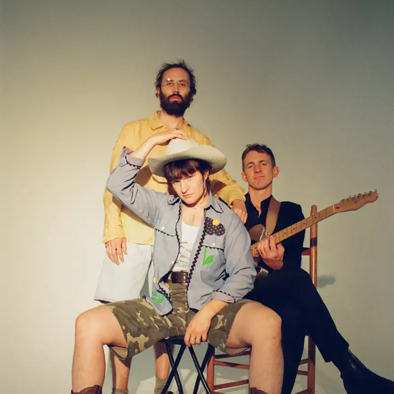 Three members of Big Thief on a white background. Adrianne Lenker is wearing a white cowboy hat.