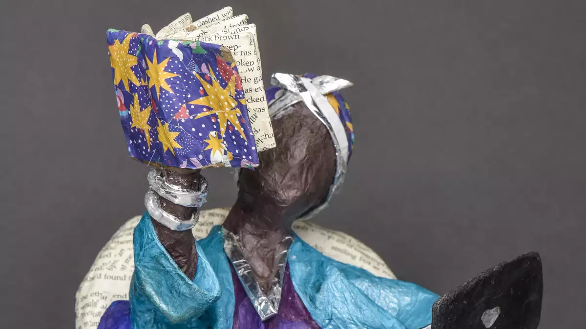 A papier mache figure holding a papier mache book