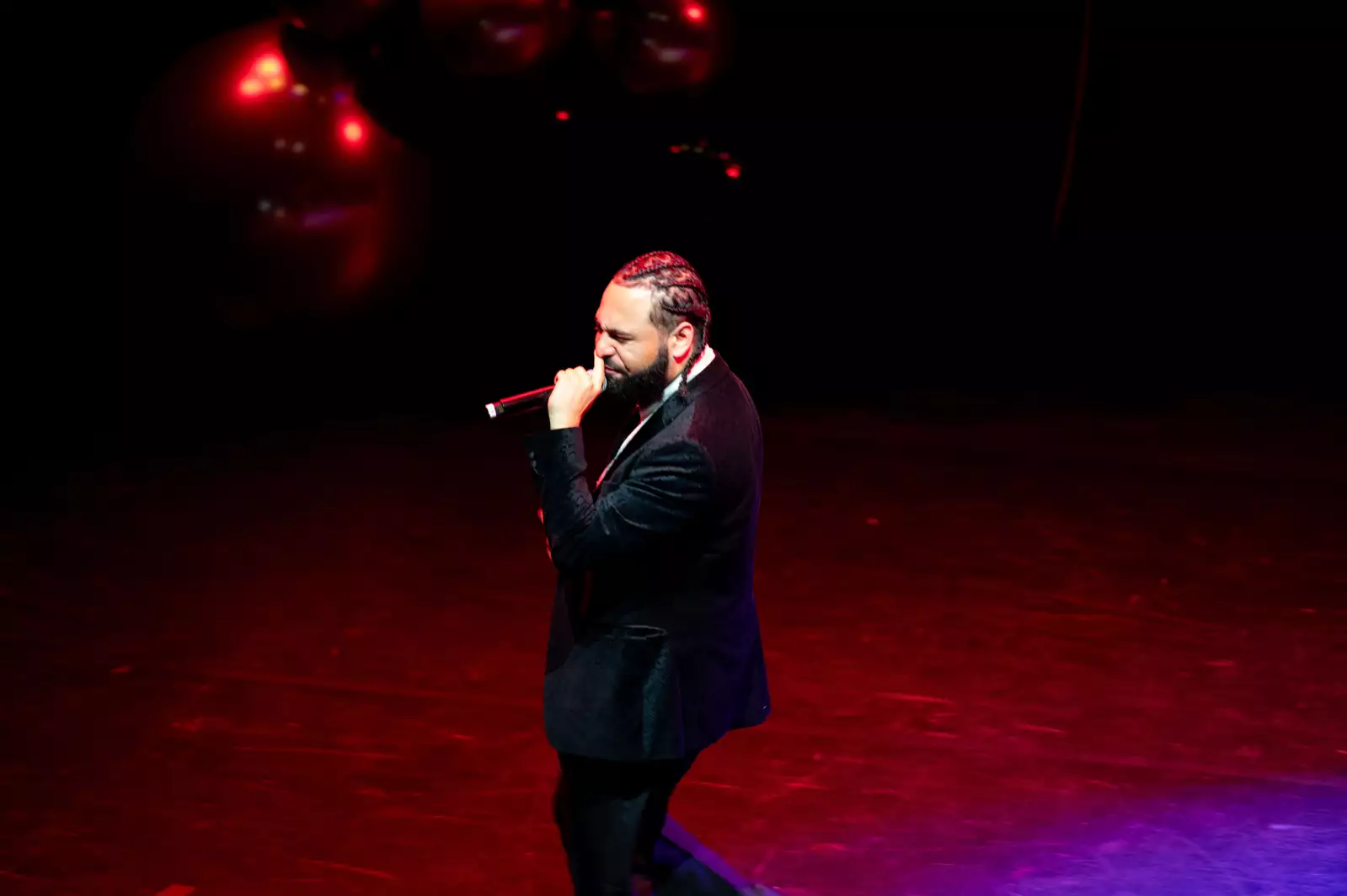 A man in a black velvet suit sings into a microphone on stage at Black Creative Trailblazes. The lighting is red.