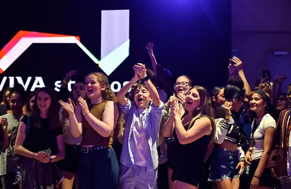 A cheering crowd of young people celebrate enthusiastically in the Social, with a glowing "Aviva Studios" sign in the background.