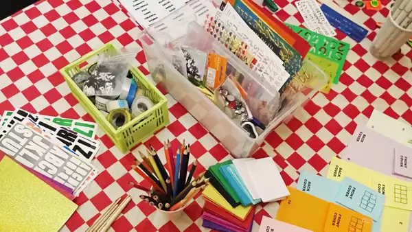 A craft table with red and white chequered table cloth, pencils and crafts