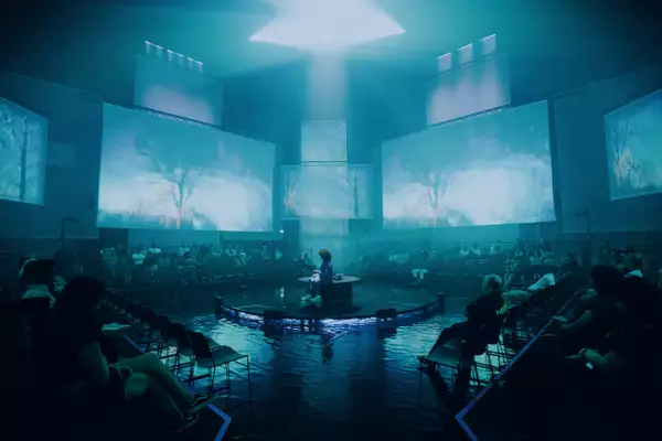 The set of A Symphony of Flesh and Bones in the Warehouse, showing projections on large screens and pieces of fabric. The lighting is blues-green.
