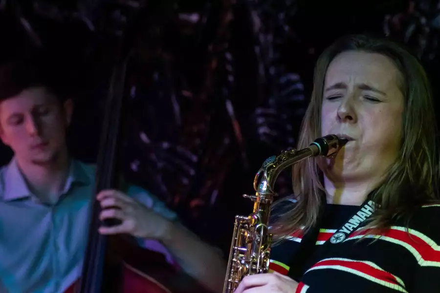 A person playing saxophone next to another playing cello
