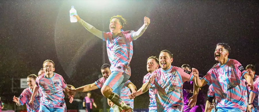 Players laughing and running on an outdoor football pitch wearing pink and blue TRUK United football kits