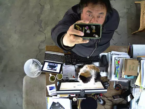 Ai Weiwei filming himself on a phone camera from above, next to a desk