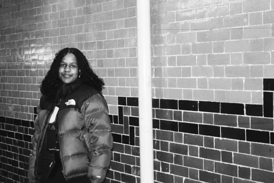 Black and white photo of a person stood against a wall smiling