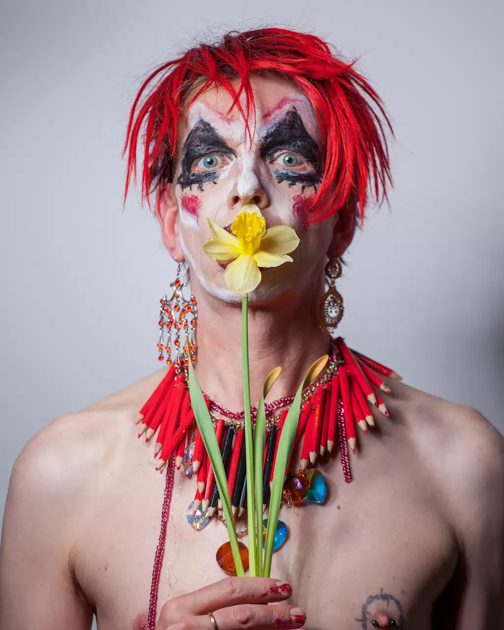 David Hoyle with bright red hair and a necklace made of red pencils, holding a daffodil