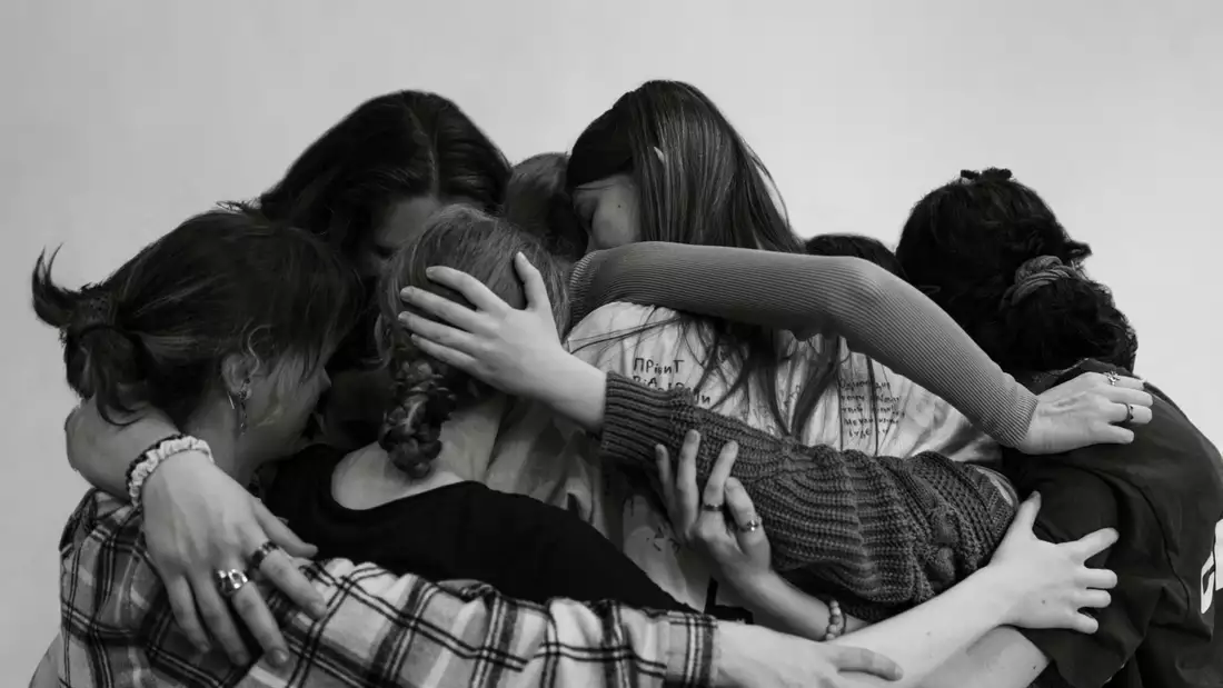 A black and white photograph of young people with their arms around each other in a group cuddle