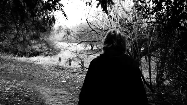 black and white photo of a woman walking through a forest