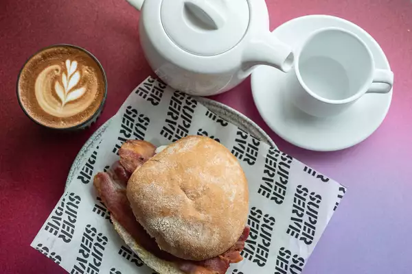 A bacon sandwich and teapot with mug