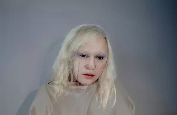 Headshot of Anohni with blonde hair, stood in front of a white wall