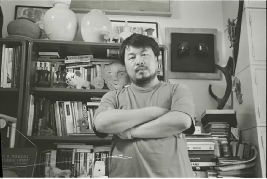 Black and white photograph of Ai Weiwei stood in front of a bookshelf