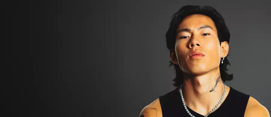 Winson wearing a black vest top and chain on a grey background