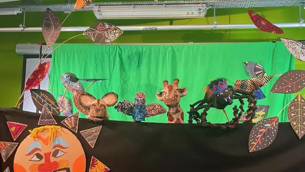 An animal puppet show against a bright green background – featuring a large spider and giraffe among other animals