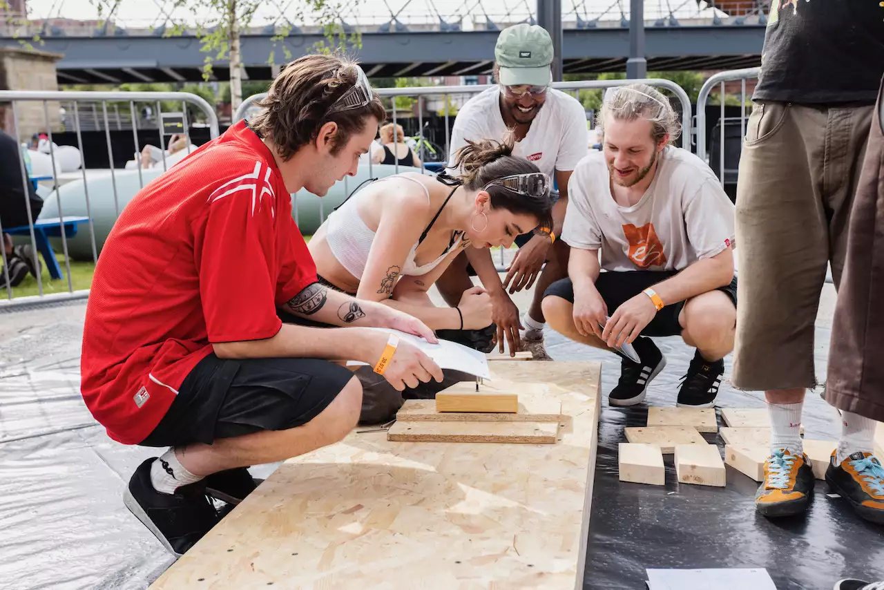 Four people working on a wooden bench as part of a skateboard ramp building workshop outside Aviva Studios for Build Manchester