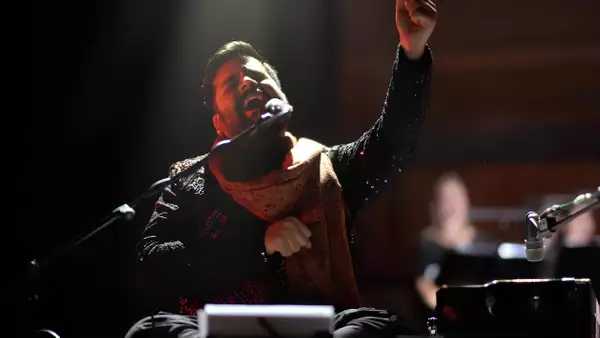 Sarthak Kalyani singing into a microphone with eyes closed and one arm raised in the air