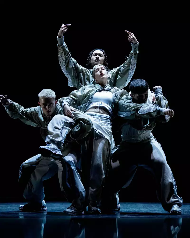 A group of five performers dancing on stage during CYCLES, dressed in loose-fitting, modern streetwear, against a dark background.