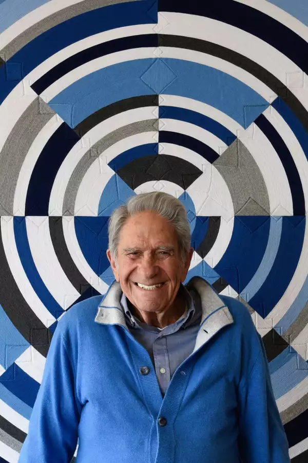 Eduardo Terrazas smiling and wearing a blue cardigan. Behind is a geometric patterned wall in different shades of blue and black.