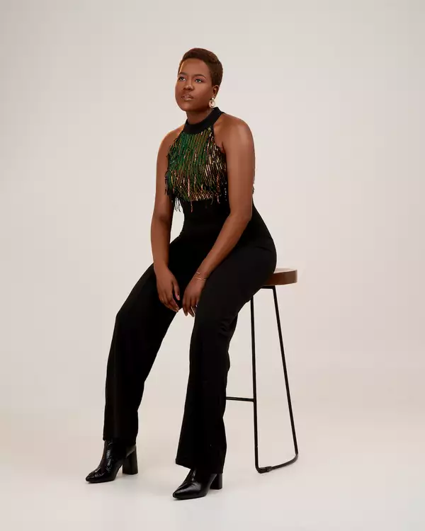 Rumbi Tauro sat on a black high stool wearing a sparkly top and black trousers