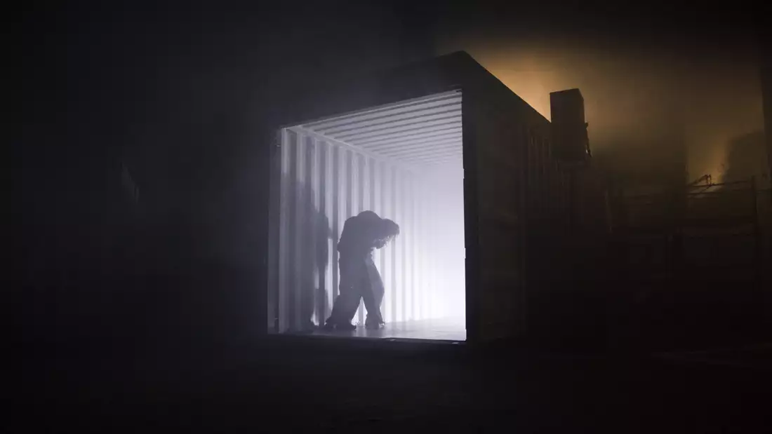 A photo of a dark warehouse space and a person stood silhouetted against a bright light coming from a shipping container
