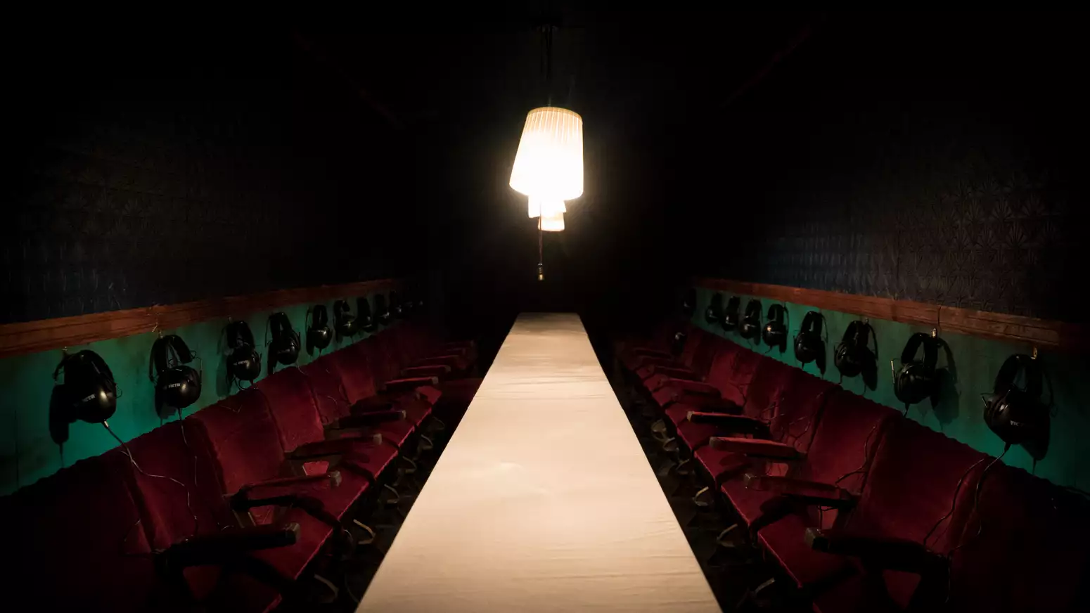 The inside of the experience séance. Showing a dimly lit container, dark red seats and an old fashioned lamp with spooky atmosphere.