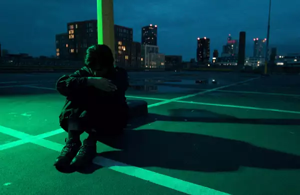 A person sat on a carpark roof at night, with a city skyline behind them