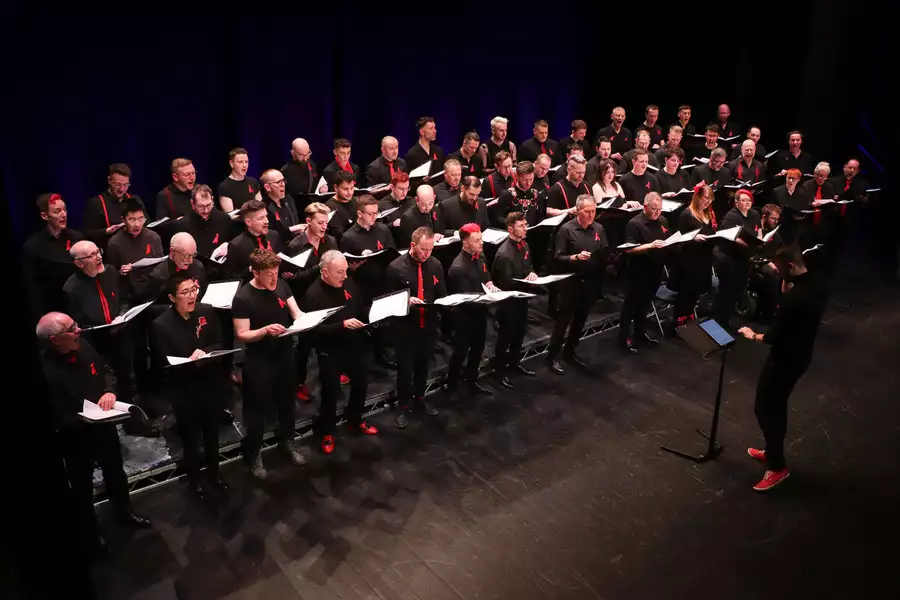 The Sunday Boys Stand in rows on a stage in front of choir director