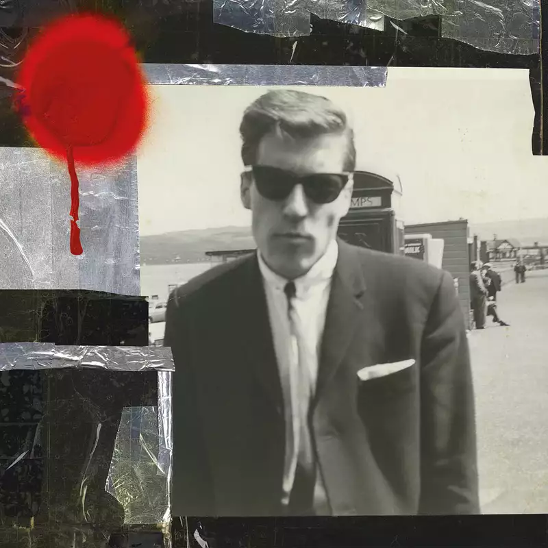 A black-and-white photo of a man wearing sunglasses and a suit, with a blurred background of a seaside scene. There is a bright red circle of paint on the photograph.