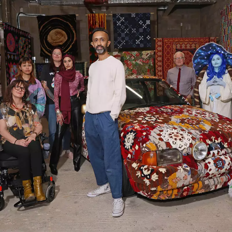 Hetain Patel standing in an exhibition with his artwork made from a car, with other people around him