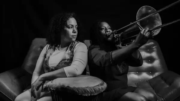 Black and white photo of two members of Ladies of Midnight Blue. One is playing a trombone.