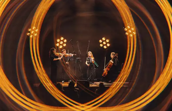 Four members of Manchester Collective perform on stage surrounded by blurred lighting