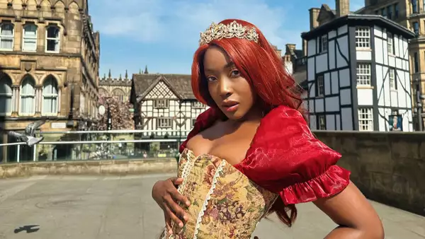 B!TEZ wearing a red dress and patterned corset, stood outside