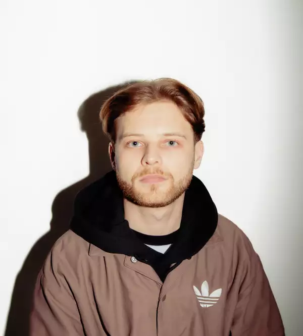 Oscar Cloud wearing a back hoodie and brown Adidas jacket, on a white background