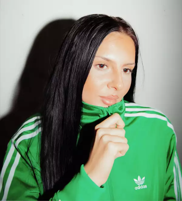 Angelica Giles wearing a green Adidas tracksuit top zipped up, on a white background